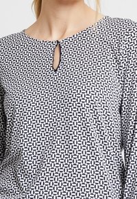 Gemusterte Bluse in Schwarz und Weiß mit einem geometrischen Druck, Rundhalsauschnitt mit einem Schlüssellochdetail und langen Ärmeln.