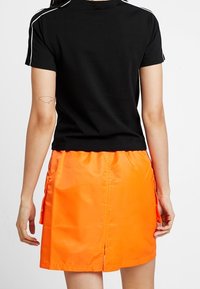 Camisa negra de manga corta con rayas blancas, combinada con una mini falda naranja brillante que cuenta con bolsillos laterales y una abertura en la parte trasera.