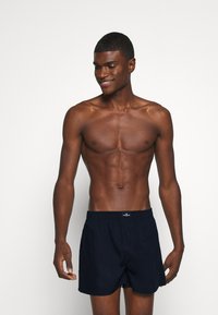 Shorts de bain bleu marine avec une taille élastique et un détail de bouton à l'avant, offrant une coupe décontractée et une texture de tissu lisse.