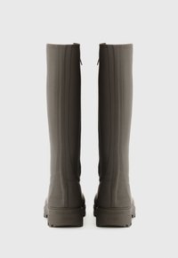 Bottes en caoutchouc grises, montantes jusqu'au genou, avec une surface texturée, des rainures verticales et des talons rectangulaires, dotées de languettes à l'arrière pour un enfilage facile.