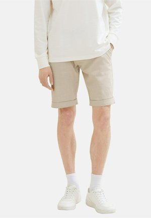 Beige shorts med struktureret stof, opkrogede kanter og sidelommer, kombineret med hvide sneakers og mellemlange sokker.