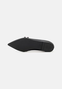 Zapato negro de punta afilada con un material superior suave, diseño minimalista, suela plana y doble correa para un detalle adicional.