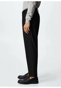 Zwarte op maat gemaakte broek met een rechte pasvorm, voorzien van een gladde afwerking en zijzakken. Gecombineerd met zwarte instappers en een grijze trui.