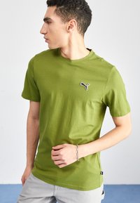 Olivengrøn bomulds T-shirt med korte ærmer, rund hals og et lille sort Puma-logo på venstre bryst. Glat tekstur, afslappet pasform.