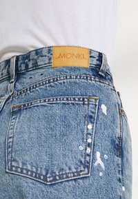 Jeans in denim azzurro chiaro con patch in pelle del logo MONKI, caratterizzati da schizzi di vernice bianca e dal classico design a cinque tasche.