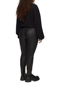Zwarte oversized trui met textuurbreiwerk, gecombineerd met strakke zwarte neplederen broeken met achterzakken, en stevige zwarte combatboots.