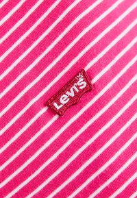Růžovo-bíle pruhovaná látka s texturovaným povrchem; obsahuje malou maroon nášivku loga Levi's.