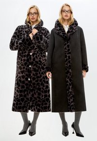 Două paltoane lungi afișate unul lângă altul: unul cu un imprimeu animal în nuanțe de negru și gri, iar celălalt solid negru cu o căptușeală cu imprimeu de leopard.