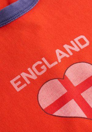 Tela roja con la palabra "ENGLAND" y un emblema en forma de corazón con la Cruz de San Jorge debajo, con un borde morado en el cuello.