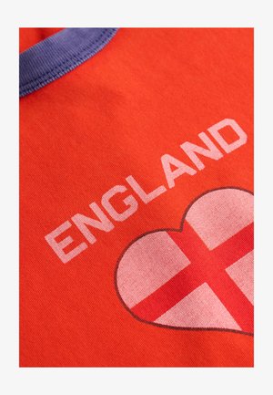Tela roja con la palabra "ENGLAND" y un emblema en forma de corazón con la Cruz de San Jorge debajo, con un borde morado en el cuello.