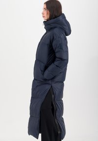 Marineblauwe pufferjas met een hoge kraag en capuchon. Voorzien van een zijrits, gestructureerde stof en een lang, geïsoleerd ontwerp.