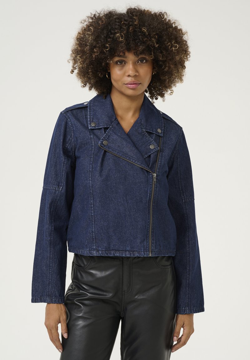 Marineblauwe denim cropped jack met een reverskraag, asymmetrische rits en drukknoopdetails. Gestyled met lange mouwen en een getailleerd ontwerp.