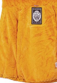 Yellow faux fur jacket featuring a black label with decorative design and size, emphasizing its soft texture and vibrant color.