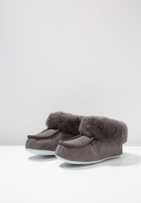 Pantofole indoor grigie con esterno in suede e un morbido polsino in pelliccia grigia. Suole piatte leggermente arrotondate, con cuciture decorative sulla parte superiore.