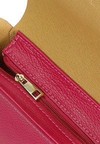 Chiusura con zip in pelle rosa con hardware dorato, che mostra una superficie texturizzata. All'interno presenta una fodera liscia color beige.