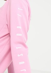 Sudadera rosa de manga larga con tejido texturizado, que presenta "JUST DO IT" en texto blanco vertical a lo largo de la manga derecha.