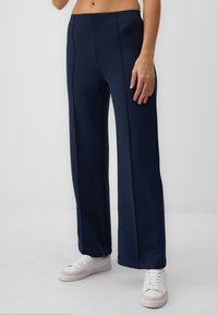 Navy wide-leg pants with a high waistband, featuring vertical seam detailing and smooth, stretchy fabric. Worn with white sneakers.