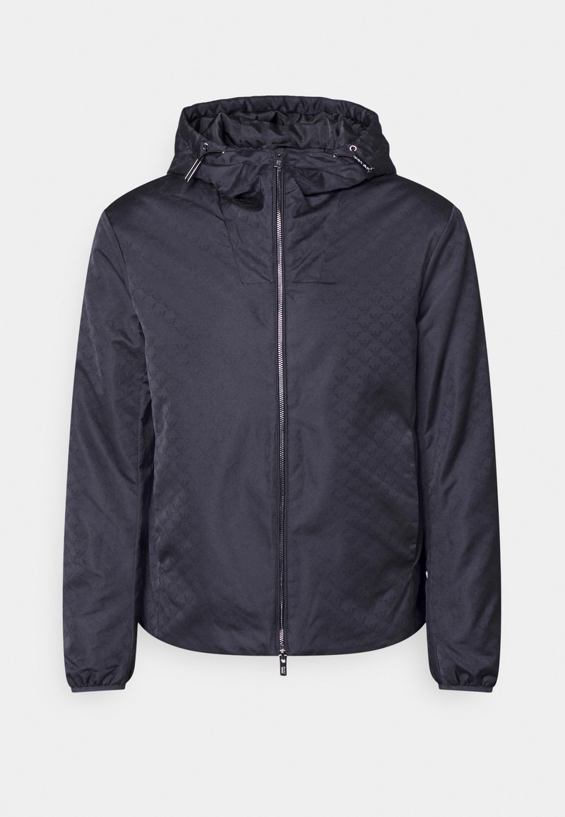 Black hooded jacket in lightweight material with a texture pattern. Features a front zipper and elastic cuffs for a secure fit.