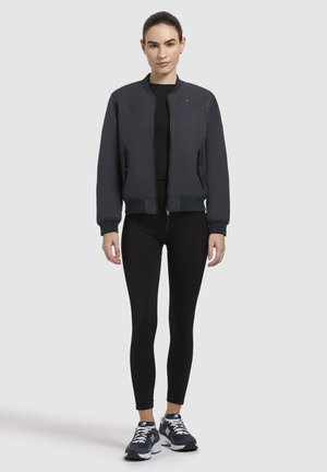 Marine bomberjack met een rits aan de voorkant, geribbelde manchetten en zoom. Gedragen over een zwarte top en gecombineerd met zwarte leggings en marineblauwe sneakers.