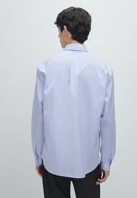 Camicia a strisce blu chiaro con maniche lunghe, colletto con bottoni e orlo arrotondato. Il tessuto sembra leggero e liscio.