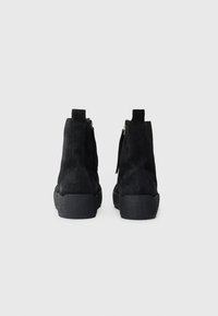 Bottines en suède noir avec une surface texturée, dotées d'une fermeture éclair arrière et d'une semelle en caoutchouc épaisse, conçues pour le confort et le soutien.