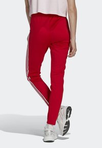 Röda joggerbyxor med en avsmalnande design, prydda med vita sidostreck och en elastisk midja, tillsammans med vita sportskor.