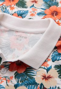 Blommig polo tröja med färgglad hibiskus och lövmönster. Vit ribbad krage och knappar. Lättviktig tyg med livfulla färger.