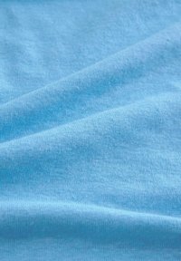 Tessuto di cotone azzurro chiaro con una superficie liscia, caratterizzato da sottili variazioni di colore e leggerissime ondulazioni dovute alla sua forma piegata.