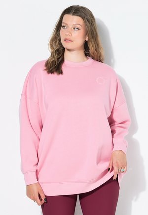 Světle růžová oversized mikina s kulatým výstřihem a dlouhými rukávy; má malé logo na hrudi a elasticizované manžety a spodní lem.
