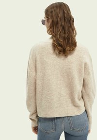 Licht beige wollen blend pullover trui met een relaxte pasvorm, geribde halslijn en lange mouwen, gecombineerd met hoge taille blauwe spijkerbroek.