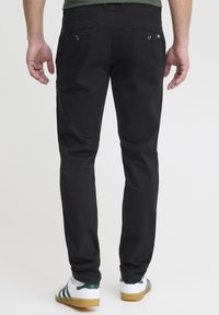 Zwarte broek met een slim fit, voorzien van twee achterzakken en subtiele hardware details. Gladde textuur met een clean design.