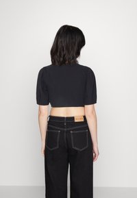 Crop top noir en tissu texturé avec des manches courtes bouffantes, associé à un pantalon noir taille haute doté de coutures blanches et d'un patch logo.