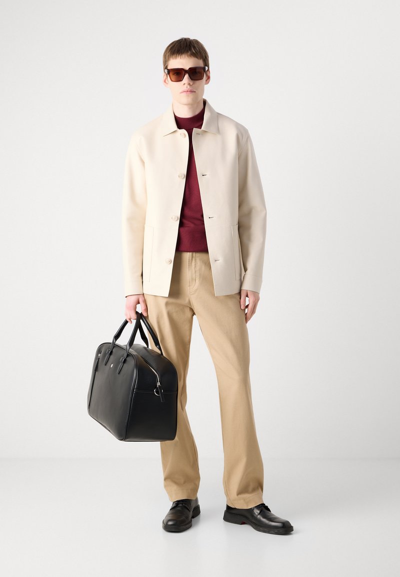Lichtbeige jas, bordeauxrode coltrui, beige broek, zwarte leren tas en zwarte schoenen. Vierkante zonnebril maakt de look compleet.