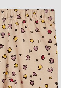 Bamboe stoffen leggings in beige met een elastische tailleband. Kenmerkt zich door verspreide hartvormige patronen in zwart, geel, paars en rood.