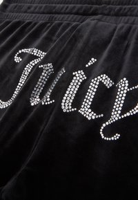 Melni samta sporta bikses ar "Juicy" logotipu, kas rotāts ar spīdīgiem rhinestones, ar gludu tekstūru un elastīgu jostu.