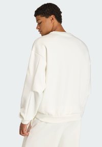 White crewneck sweatshirt with a relaxed fit, dropped shoulders, and ribbed cuffs. Smooth, soft fabric with no visible patterns or accents.
