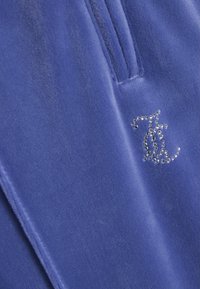 Niebieski materiał welurowy z detalem w postaci zamka i ozdobnym srebrnym logo z kryształków. Gładka faktura o miękkim połysku.