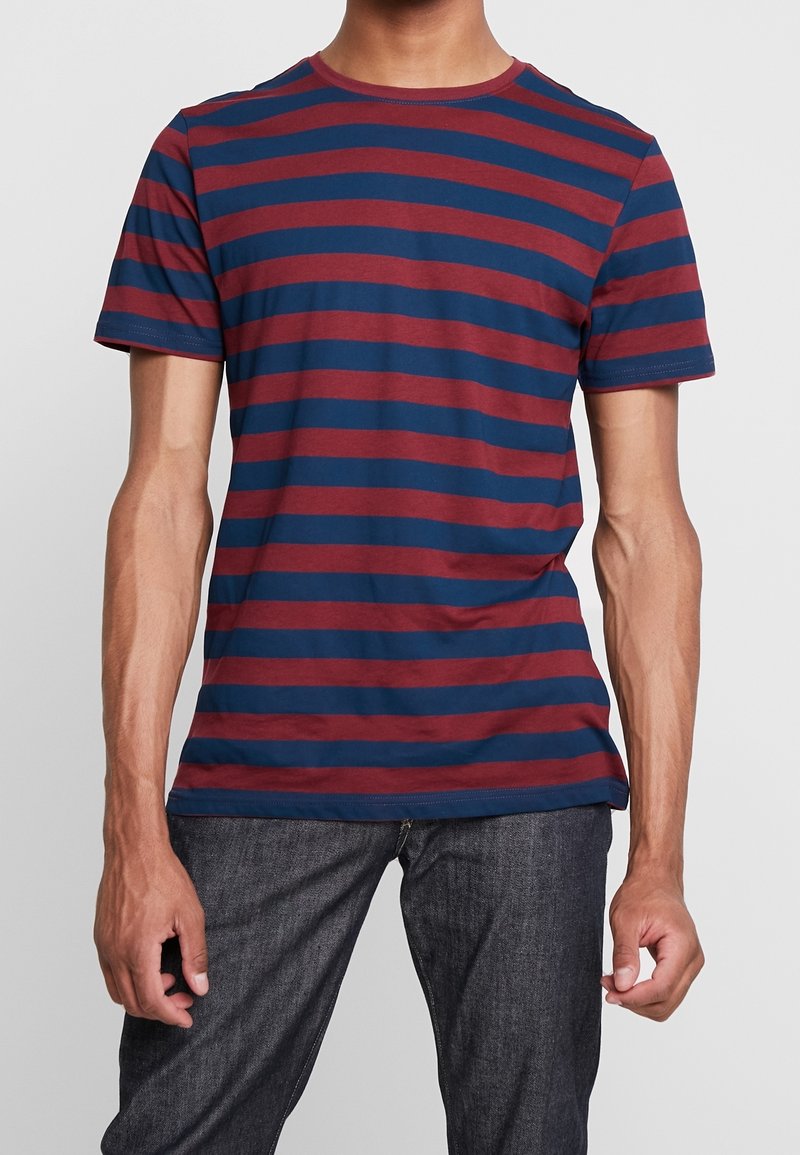 T-shirt à rayures aux couleurs bleu marine et bordeaux, manches courtes, col rond, en coton doux. Associé à un jean en denim foncé.