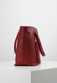 Czerwona skórzana torebka na ramię o teksturowanym wykończeniu, z dwoma uchwytami i boczną kieszenią na zamek. Torebka ma usztywniony kształt i płaskie dno.