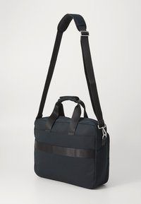 Czarna torba na laptopa wykonana z tkaniny, z podwójnymi uchwytami u góry, regulowanym paskiem na ramię, eleganckim designem i poziomym błyszczącym paskiem akcentującym.