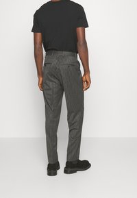 Szare spodnie w prążki o dopasowanym kroju, z tylnymi kieszeniami, szlufkami na pasek i gładką fakturą materiału. Połączone z czarnym obuwiem.