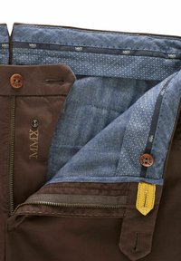 Pantalons marron avec un intérieur en denim bleu contrastant, présentant un motif en chevron et des accents jaunes. Fermeture à glissière et à bouton sont présentes.
