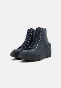Baskets montantes en matériau texturé bleu foncé avec une semelle compensée, œillets dorés et lacets noirs. Comprend une pointe arrondie et une semelle en caoutchouc.