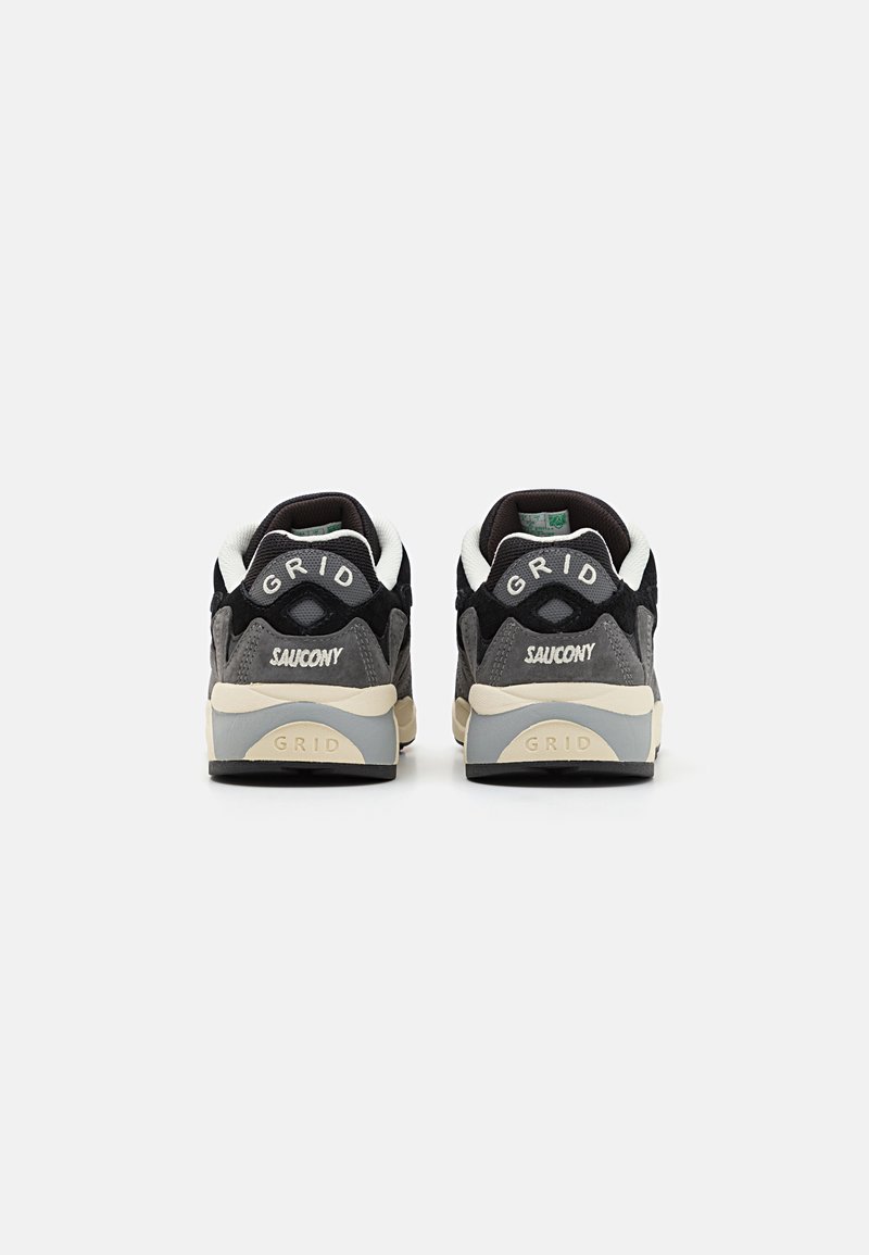 Sneaker in suede nero e grigio con accenti beige, dotati di branding "GRID" e "SAUCONY" sul tallone. Materiali testurizzati migliorano la presa.