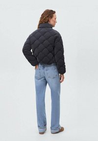 Doudoune noire matelassée avec un col montant, présentant un motif circulaire texturé. Associée à un jean en denim droit bleu clair.