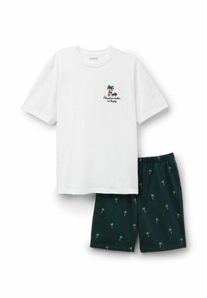 Biała koszula z krótkim rękawem z napisem "Przygoda mnie uszczęśliwia" oraz grafiką palmy, zestawiona z ciemnymi szortami z drobnym wzorem palm.