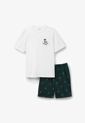 Biała koszula z krótkim rękawem z napisem "Przygoda mnie uszczęśliwia" oraz grafiką palmy, zestawiona z ciemnymi szortami z drobnym wzorem palm.