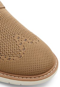 Zapato de punto color beige con una textura transpirable, puntera redondeada y una suela de goma blanca en contraste. La costura detallada acentúa el diseño.
