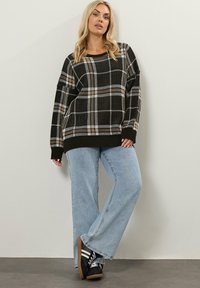 Yhdenneksilaitetta, ruskeaa ja valkoista ruutukuosisesta ylisuuresta villatakkia, jossa on resorihihat, yhdistettynä vaaleansinisiin leveälahkeisiin farkkuihin ja mustiin tennareihin, joissa on valkoisia raitoja.