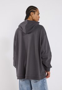 Czarnoszary, oversize hoodie w luźnym kroju, z dużym kapturem, opadającymi ramionami i prążkowanym wykończeniem, w połączeniu z jasnoniebieskimi dżinsami.